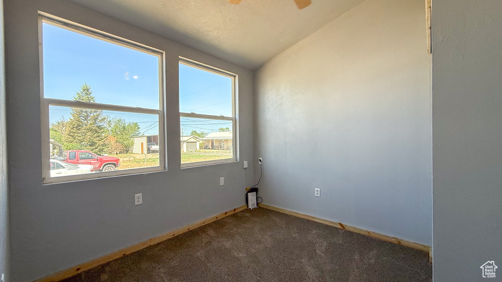 Unfurnished room with healthy amount of natural light, dark colored carpet, baseboards, vaulted ceiling, and ceiling fan