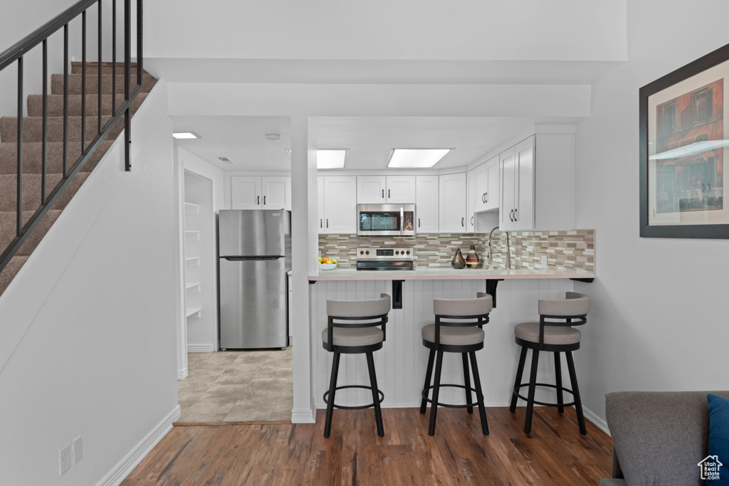 Kitchen with stainless steel appliances, decorative backsplash, white cabinets, dark wood-style floors, and light countertops