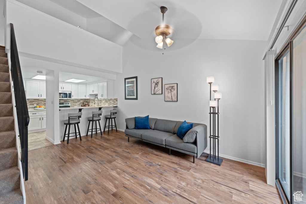Living room with stairs, light wood finished floors, a ceiling fan, baseboards, and high vaulted ceiling