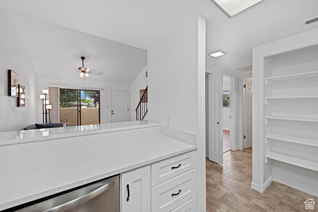 Kitchen with dishwasher, white cabinetry, a ceiling fan, and light stone countertops
