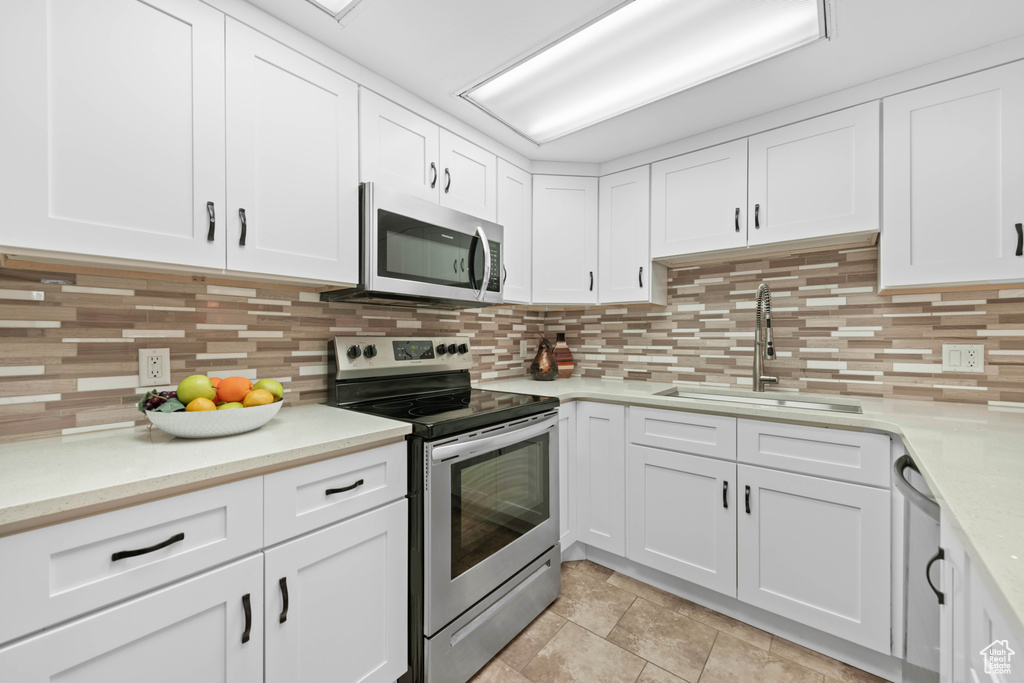 Kitchen with stainless steel appliances, a sink, white cabinetry, and backsplash