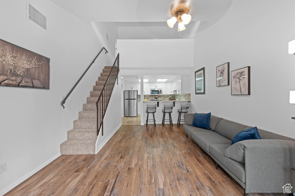 Living area featuring stairs, a ceiling fan, baseboards, wood finished floors, and a high ceiling