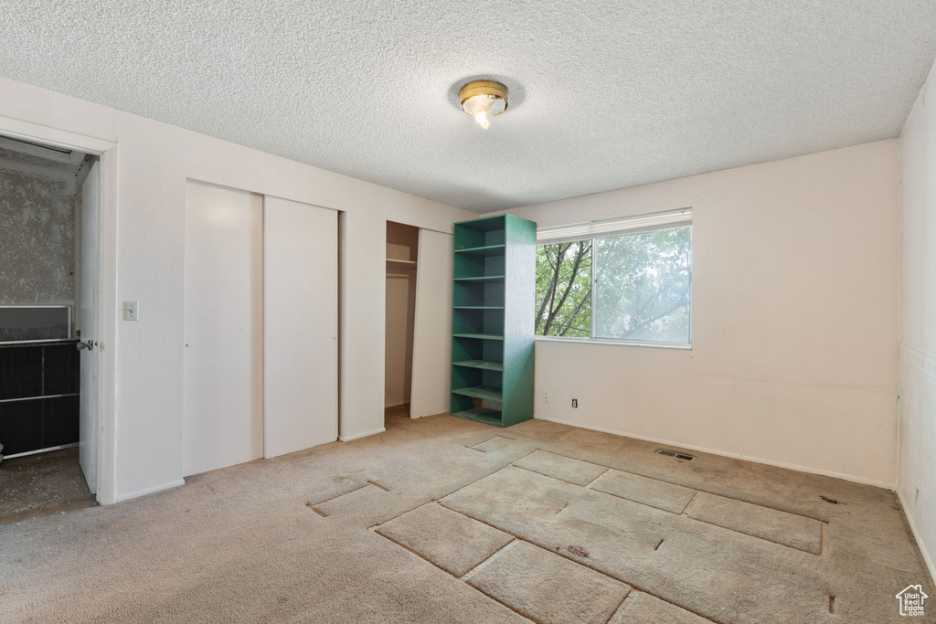 Unfurnished bedroom featuring carpet, a textured ceiling, and multiple closets