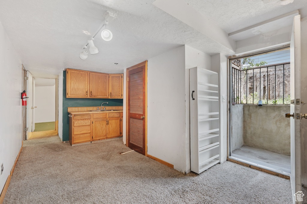 Kitchen featuring baseboards, light colored carpet, a textured ceiling, a sink, and light countertops