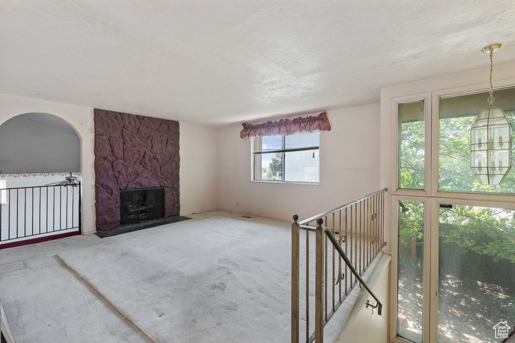 Unfurnished living room featuring carpet floors, a stone fireplace, and a textured ceiling