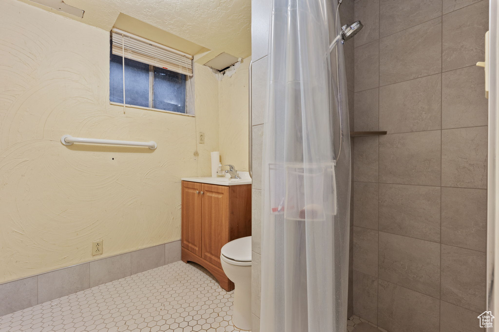 Bathroom featuring vanity, tiled shower, toilet, and tile patterned flooring