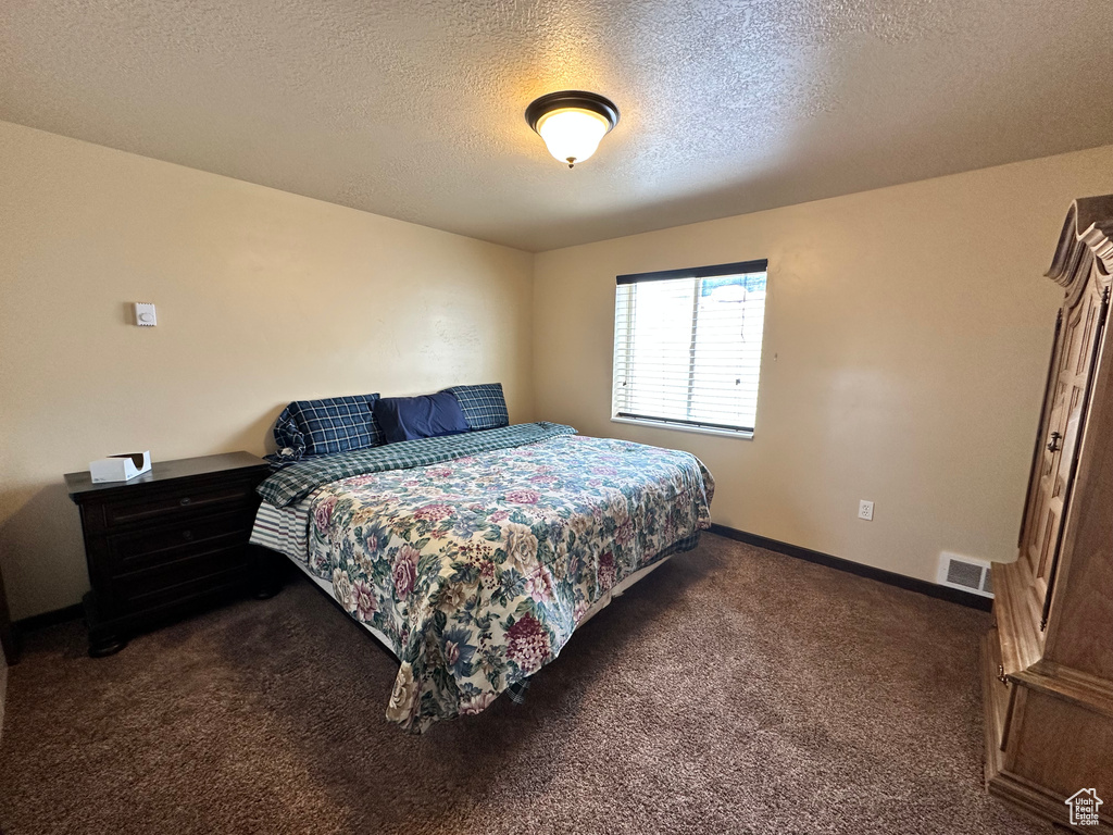 Bedroom featuring dark carpet, a textured ceiling, and baseboards