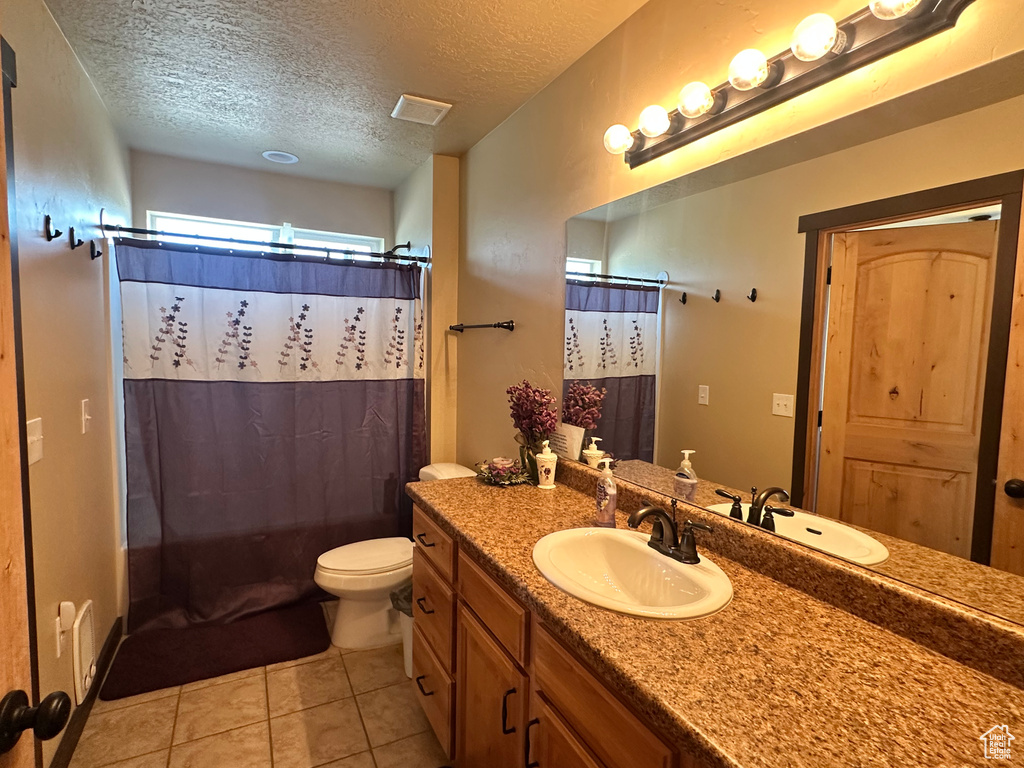 Bathroom featuring vanity, a textured ceiling, toilet, tile patterned flooring, and shower / bath combination with curtain