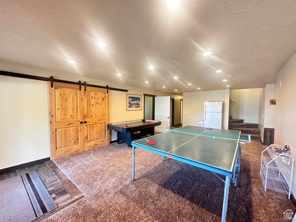 Playroom featuring a textured ceiling, dark carpet, a barn door, recessed lighting, and baseboards