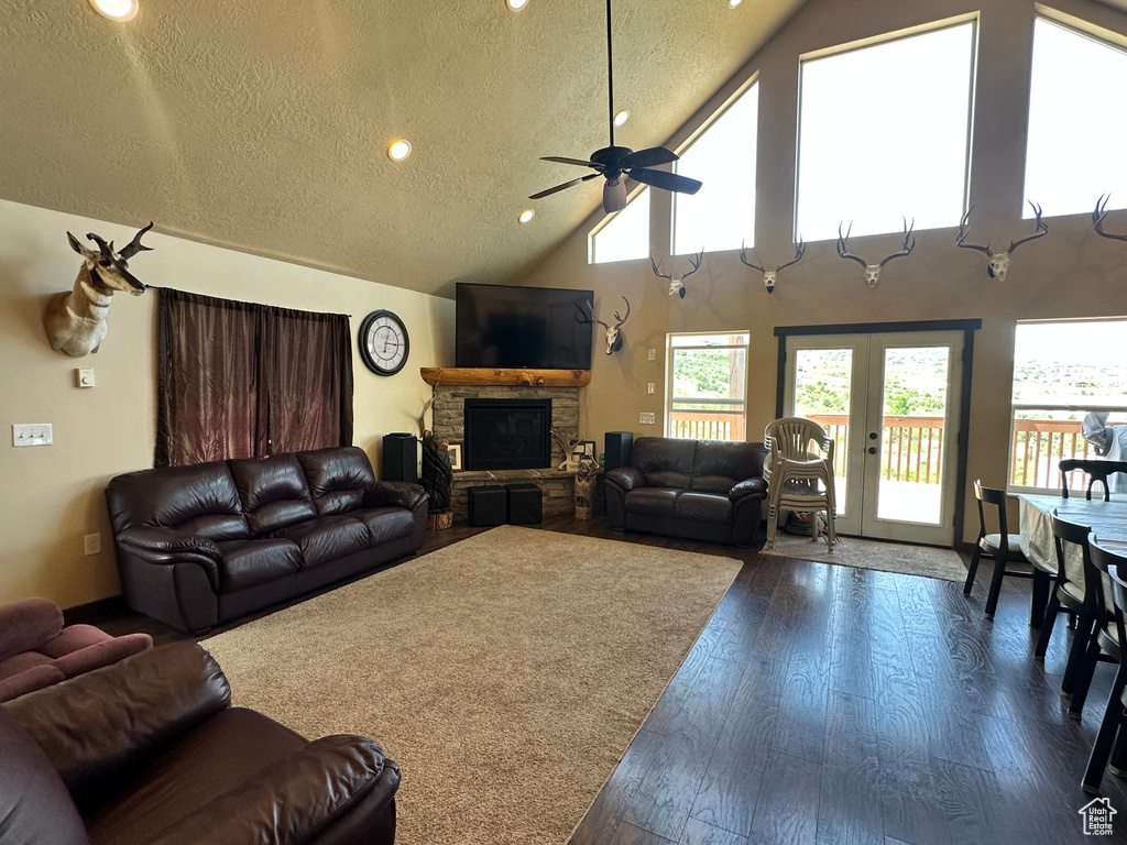 Living room with a ceiling fan, a fireplace, dark wood-type flooring, high vaulted ceiling, and a textured ceiling