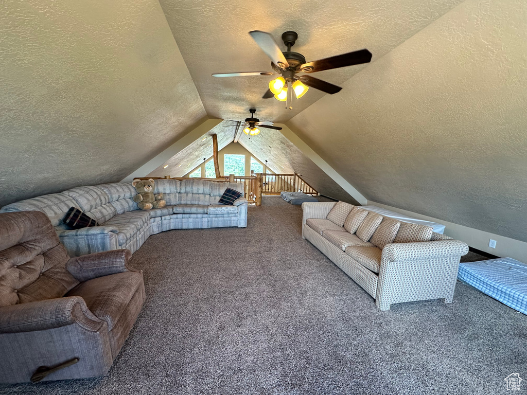 Carpeted living room featuring vaulted ceiling, ceiling fan, a textured ceiling, and a textured wall