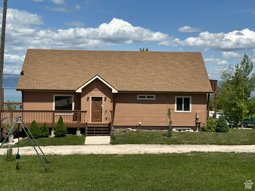 View of front of home featuring a deck, a shingled roof, and a front yard