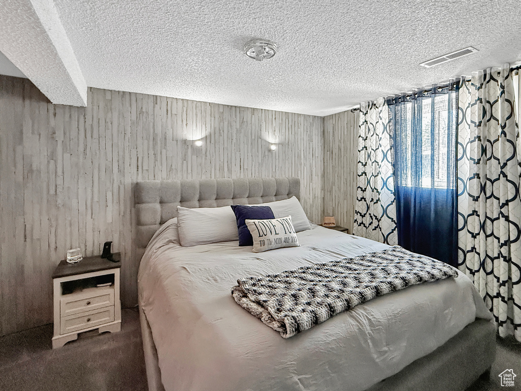 Bedroom with wooden walls, a textured ceiling, and carpet floors