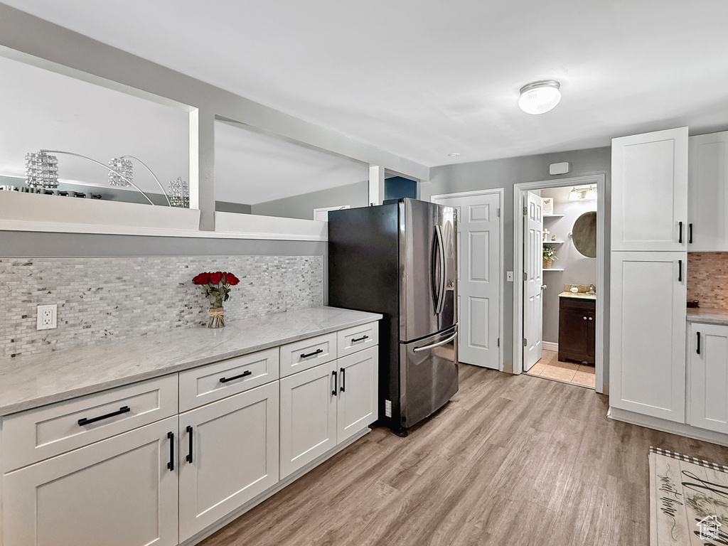 Kitchen featuring stainless steel refrigerator with ice dispenser, decorative backsplash, white cabinetry, and light wood-type flooring