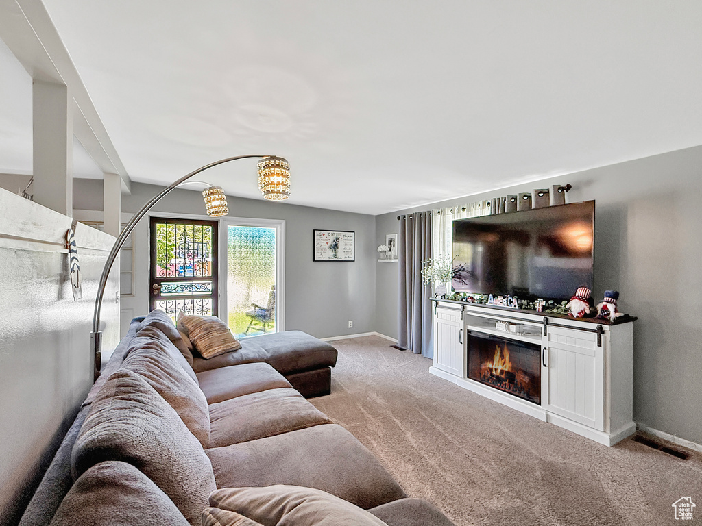 Carpeted living room featuring baseboards, a warm lit fireplace, and a chandelier