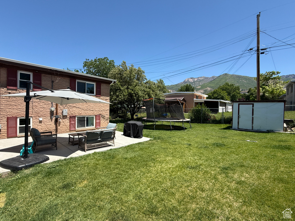 View of grassy yard featuring a trampoline, a patio area, a mountain view, and an outdoor hangout area