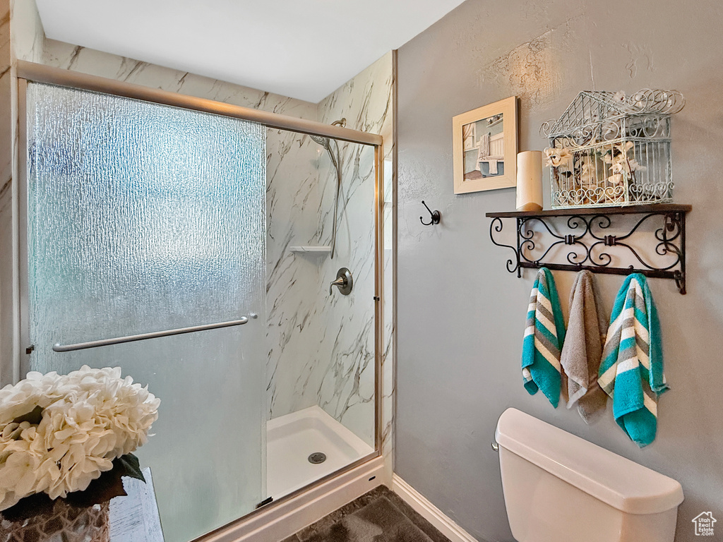 Full bathroom featuring toilet, a marble finish shower, and baseboards