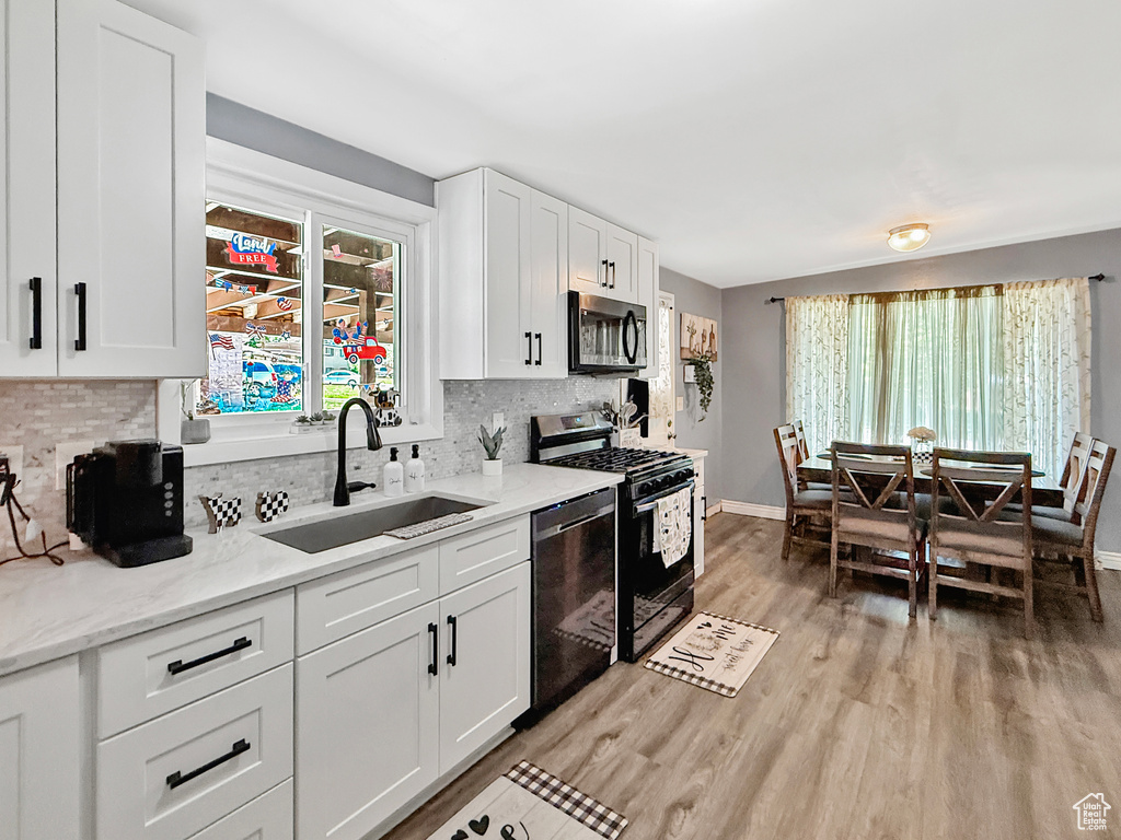Kitchen featuring appliances with stainless steel finishes, a sink, light wood-type flooring, and tasteful backsplash