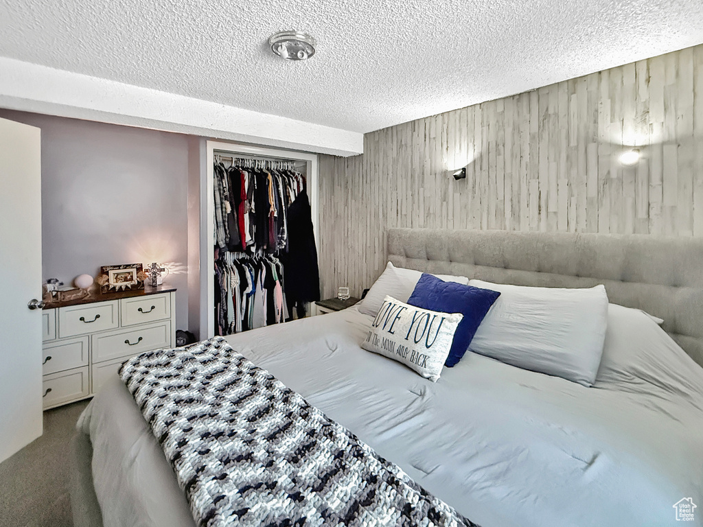 Carpeted bedroom with a textured ceiling, wooden walls, and a closet