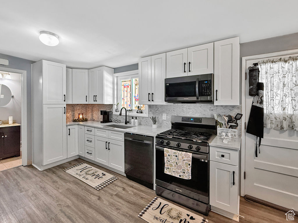 Kitchen with stainless steel appliances, a sink, light countertops, decorative backsplash, and white cabinetry