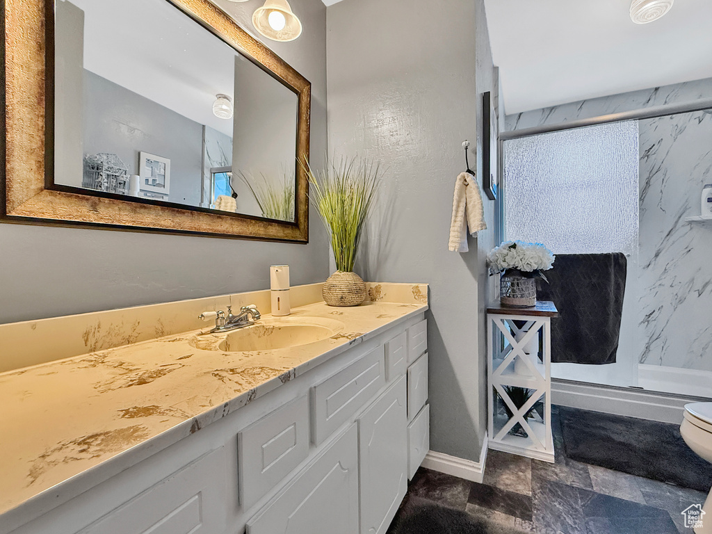 Full bathroom with vanity, a stall shower, toilet, and baseboards