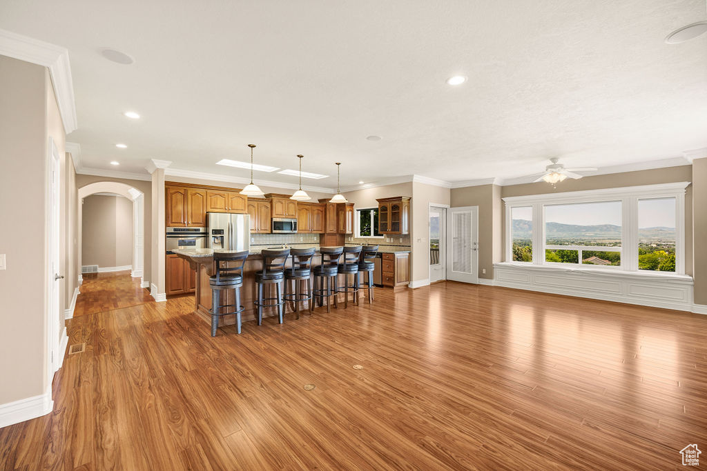 Kitchen with stainless steel appliances, a breakfast bar, a kitchen island, brown cabinets, and ornamental molding