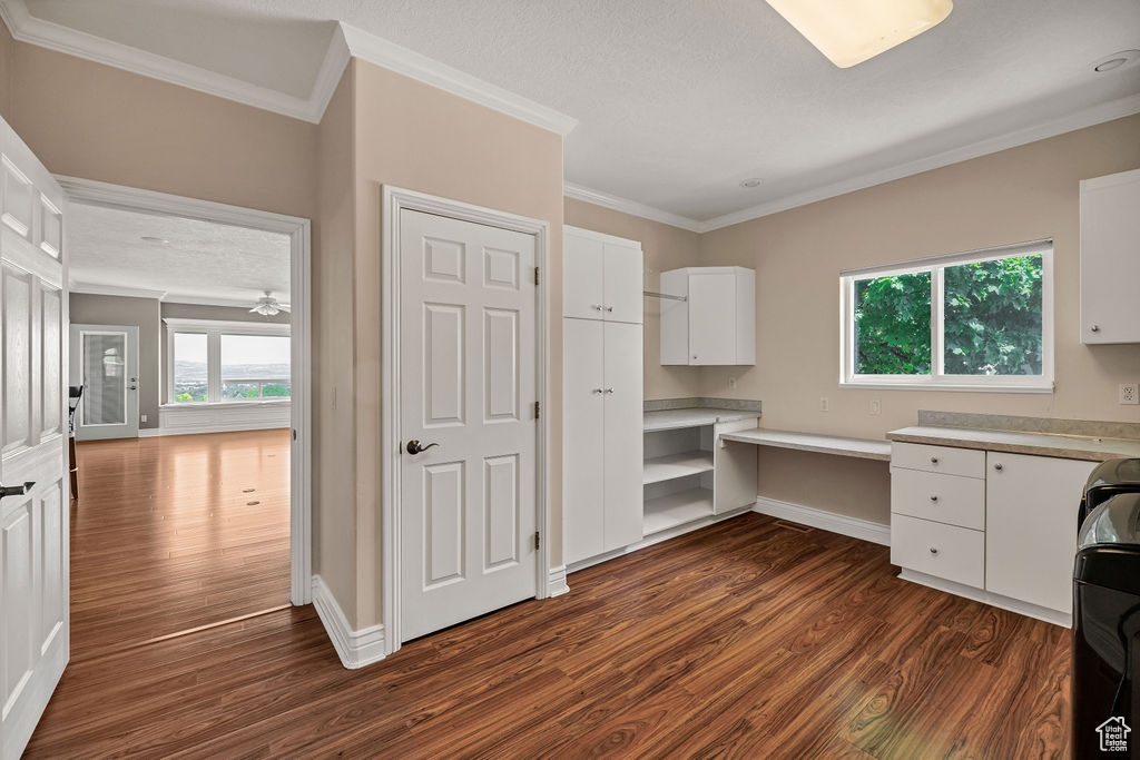 Unfurnished office with dark wood-style flooring, ornamental molding, built in study area, and baseboards