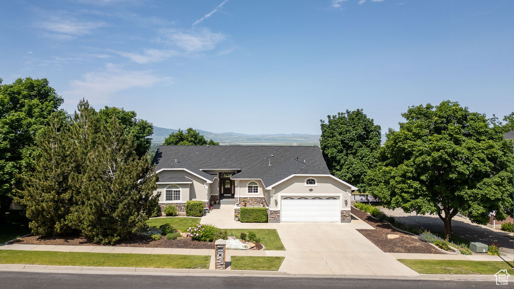 Single story home with an attached garage, stucco siding, stone siding, concrete driveway, and a mountain view