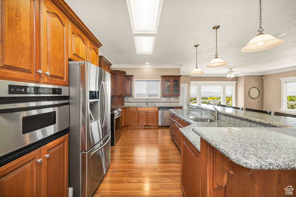 Kitchen featuring stainless steel appliances, a sink, brown cabinets, wood finished floors, and ornamental molding