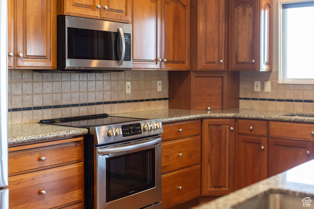 Kitchen with appliances with stainless steel finishes, brown cabinetry, decorative backsplash, and light stone countertops