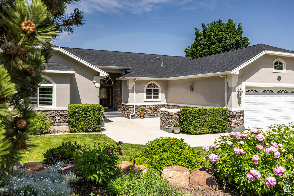 Ranch-style home featuring stone siding, stucco siding, a garage, and a shingled roof