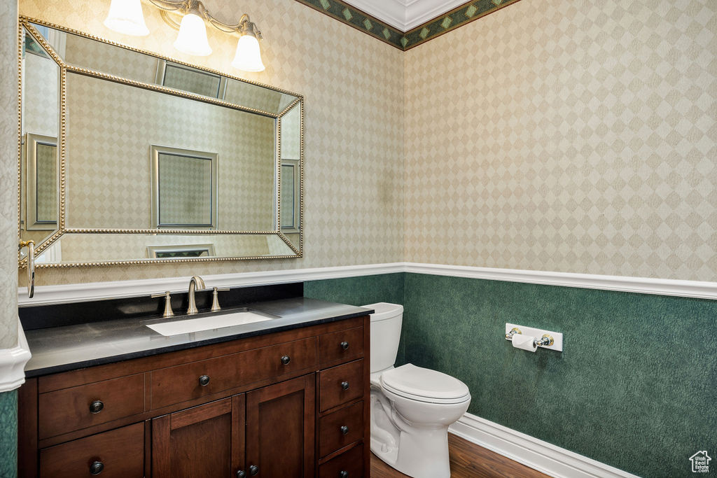 Bathroom with wood finished floors, toilet, vanity, and wallpapered walls
