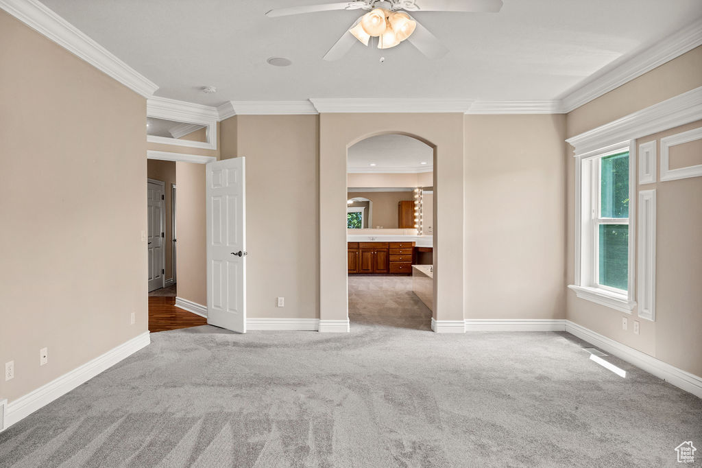 Carpeted spare room featuring arched walkways, crown molding, ceiling fan, baseboards, and a smoke detector