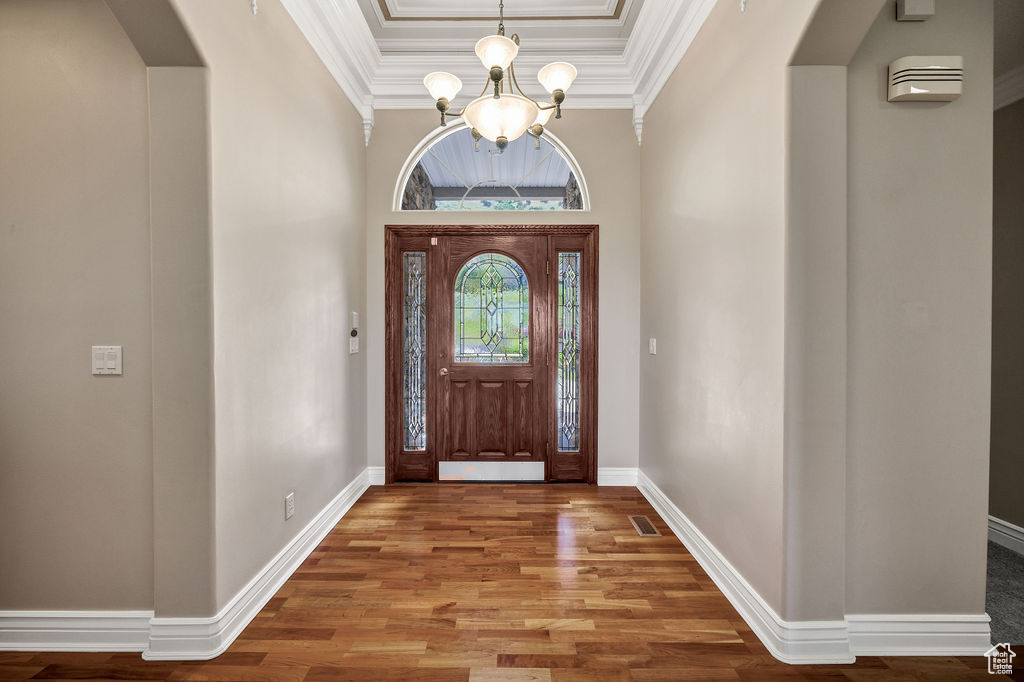 Foyer entrance featuring a chandelier, arched walkways, wood finished floors, a raised ceiling, and ornamental molding