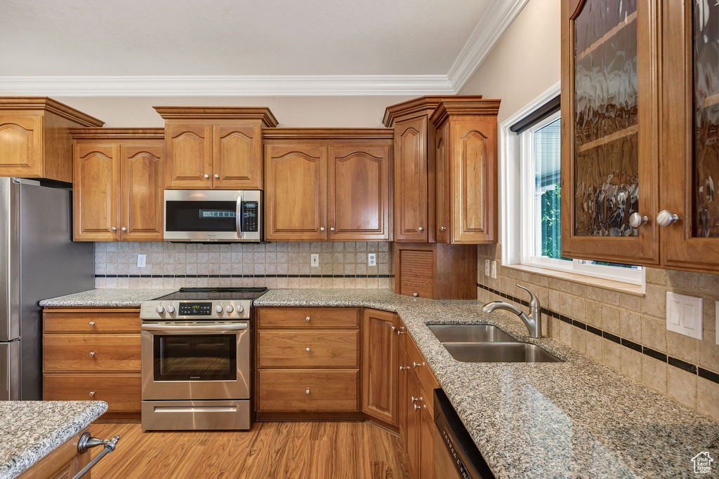 Kitchen featuring stainless steel appliances, a sink, brown cabinets, and crown molding
