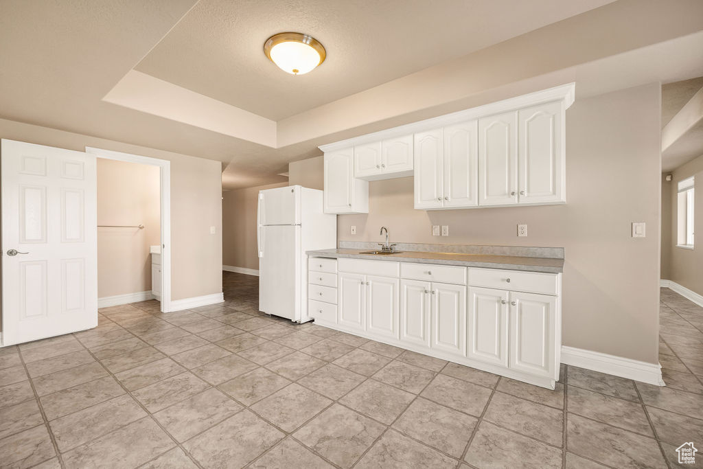 Kitchen with freestanding refrigerator, a sink, light countertops, baseboards, and a tray ceiling