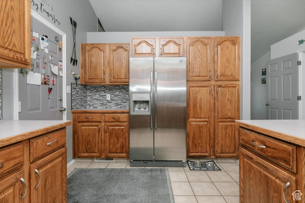 Kitchen featuring stainless steel fridge, light tile patterned floors, light countertops, and tasteful backsplash