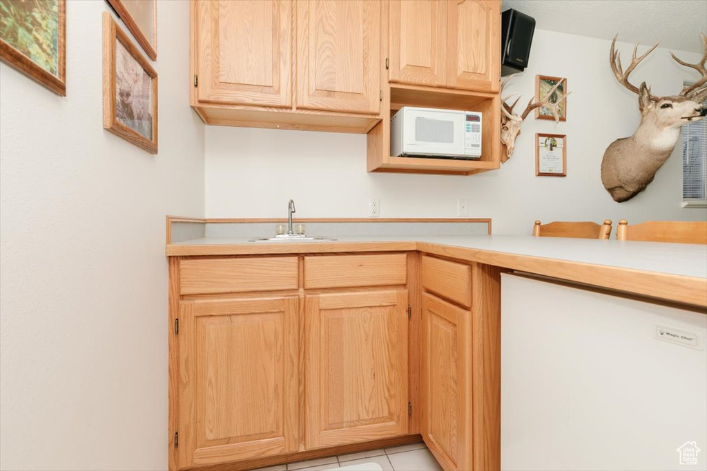 Kitchen featuring white microwave, a sink, light countertops, light brown cabinetry, and light tile patterned floors