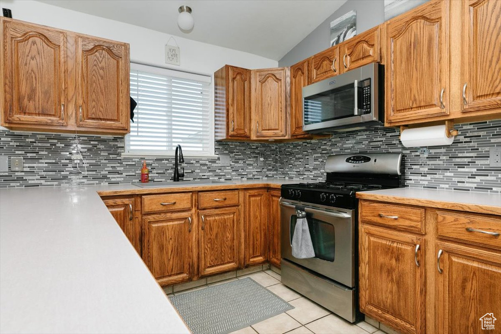 Kitchen featuring appliances with stainless steel finishes, a sink, light countertops, lofted ceiling, and tasteful backsplash