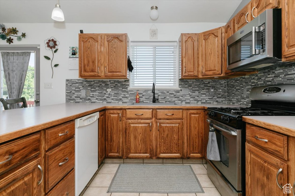 Kitchen featuring appliances with stainless steel finishes, a sink, backsplash, light countertops, and brown cabinets