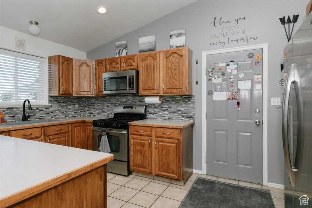 Kitchen with stainless steel appliances, a sink, light tile patterned floors, lofted ceiling, and tasteful backsplash