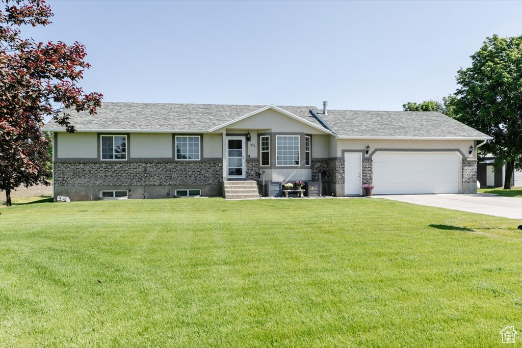 Ranch-style home featuring a garage, a front lawn, concrete driveway, and stucco siding