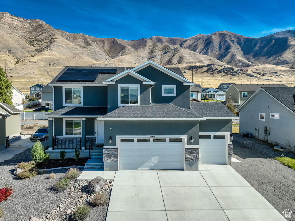 View of front of property with stone siding, stucco siding, concrete driveway, roof mounted solar panels, and a mountain view