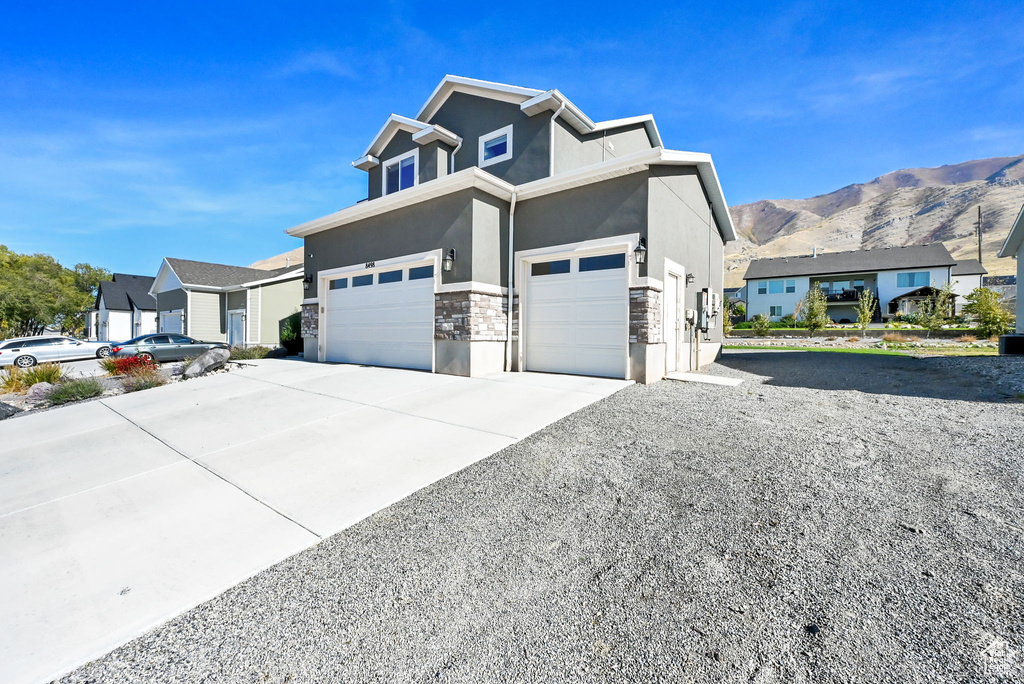 View of property exterior featuring stucco siding, stone siding, concrete driveway, a residential view, and an attached garage
