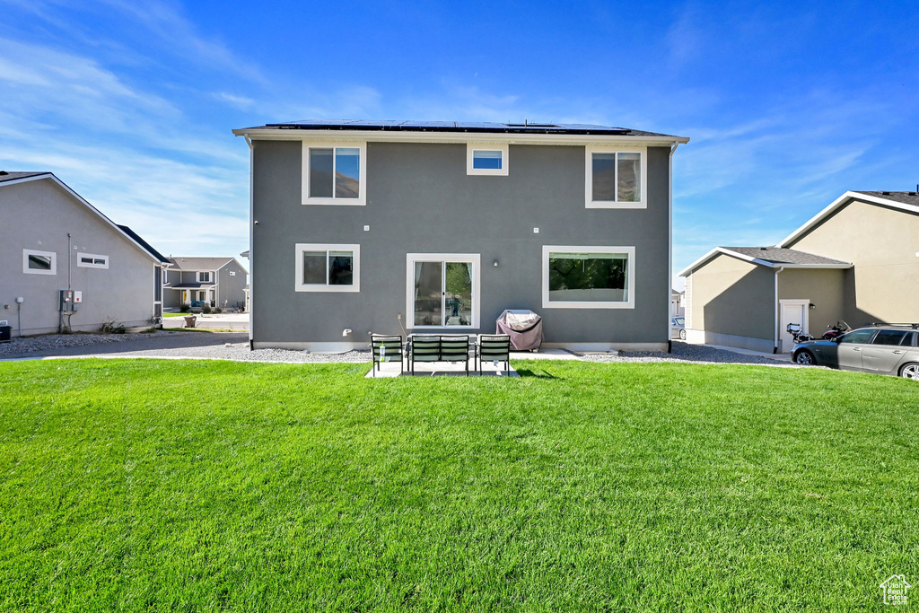 Back of house with a yard, roof mounted solar panels, and stucco siding