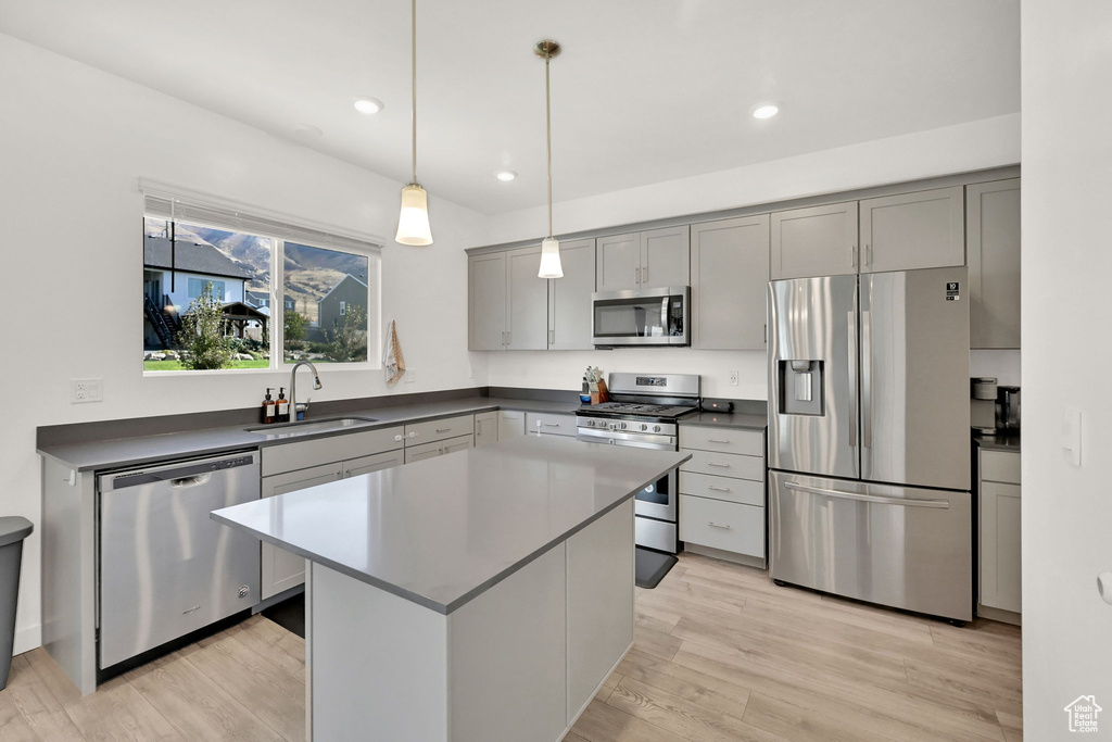 Kitchen featuring stainless steel appliances, a sink, dark countertops, light wood-style floors, and gray cabinets