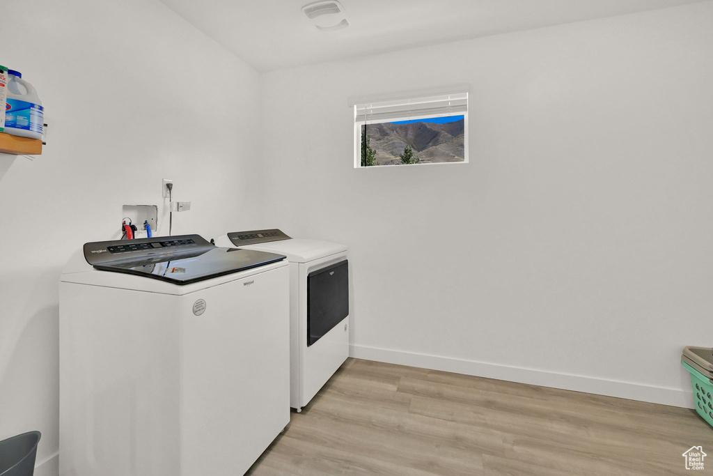Washroom with washing machine and dryer, light wood finished floors, and baseboards