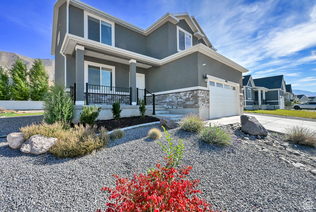 View of front of home with covered porch, stone siding, stucco siding, and driveway
