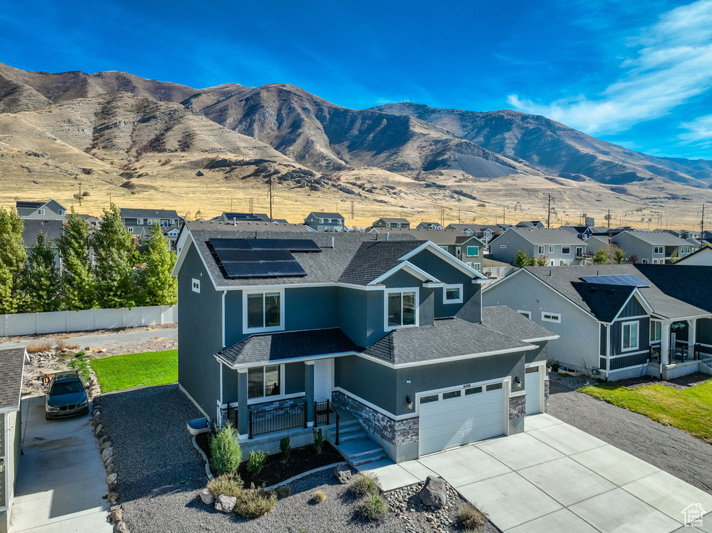 View of front of home featuring covered porch, a garage, roof with shingles, roof mounted solar panels, and stone siding
