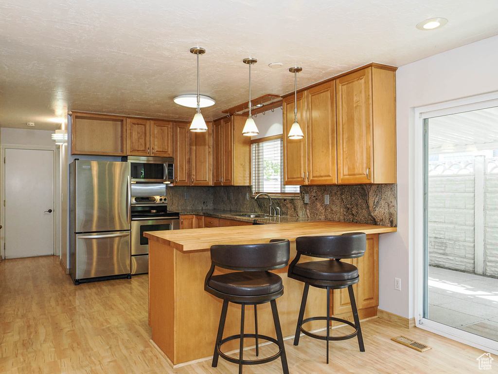 Kitchen featuring appliances with stainless steel finishes, wooden counters, a sink, and light wood-style flooring